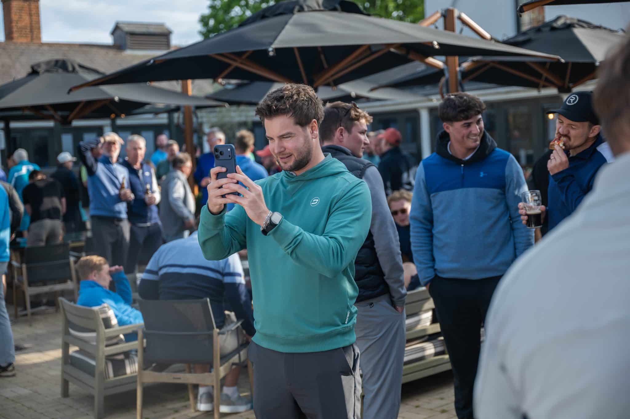 People socializing outdoors, capturing moments on a phone, illustrating the community aspect of Partnering with Engage.