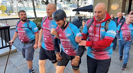 Group of men in matching jerseys supporting a participant in a charity walk, illustrating community spirit on the About Engage page.